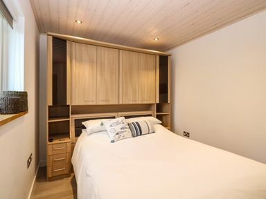 A bedroom with a double bed white bedding wooden overhead cabinets and a window with woven baskets on the sill at Links View in Fritton