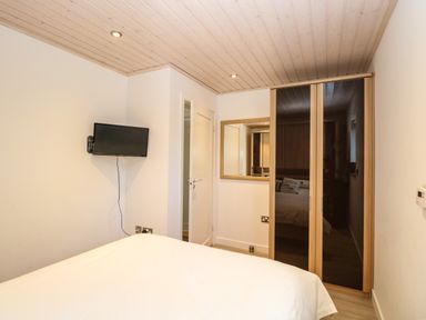 A bedroom with a bed a wall-mounted TV a mirrored wardrobe and a wooden ceiling at Links View in Fritton