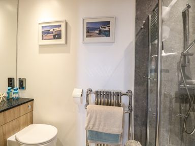 A bathroom with a toilet cabinet towels on a towel rack and a glass shower enclosure at Links View in Fritton