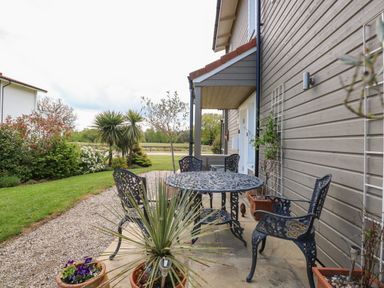 An outdoor patio area with metal table and chairs next to a house with potted plants and garden in the background at Links View in Fritton