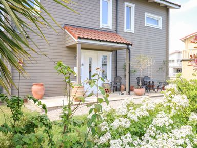 A gray house with a white door and a small covered patio with outdoor furniture and plants at Links View in Fritton