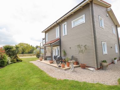 An exterior view of a two-story wooden house with a small patio area and potted plants at Links View in Fritton