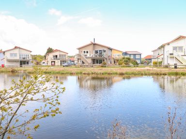 A group of houses by a lake with a tree in front at Links View in Fritton