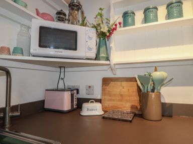 A kitchen with a microwave, toaster, and utensils container at Smugglers Cottage Trebarwith Strand near Tintagel