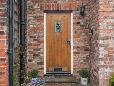 A wooden front door with a small window set in a brick wall with potted plants on either side at Manor Cottage in Northallerton