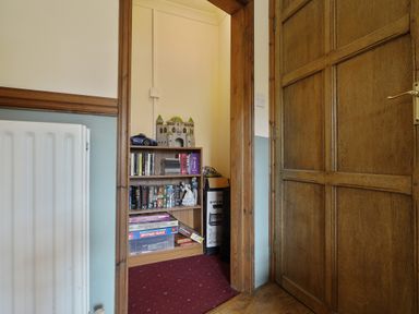 A small room with a wooden door a white radiator and a bookshelf filled with books board games and decorative items at Manor Cottage in Northallerton