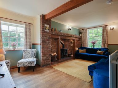 A living room with blue sofas a floral chair a brick fireplace and wooden floor at Manor Cottage in Northallerton