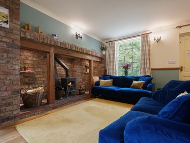 A living room with a brick fireplace and wood stove two blue sofas and a large window at Manor Cottage in Northallerton