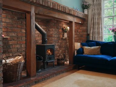 A living room with a wood burning stove fireplace a basket of firewood a blue sofa and flowers in vases at Manor Cottage in Northallerton