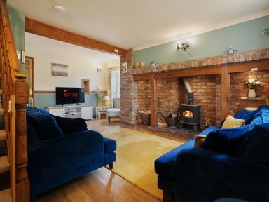 A living room with blue sofas a wood burning stove on a brick fireplace and a television showing Netflix at Manor Cottage in Northallerton