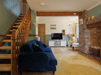 A living room with a blue sofa wooden stairs a TV showing Netflix a brick fireplace and wooden flooring at Manor Cottage in Northallerton