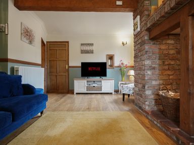 A living room with a blue sofa a TV on a white stand a wooden door and a brick fireplace at Manor Cottage in Northallerton