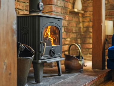 A burning wood stove with metal buckets next to it in a room with brick walls at Manor Cottage in Northallerton