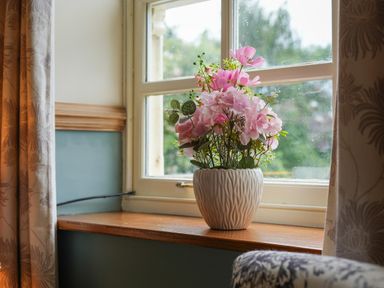 A vase with pink flowers on a wooden windowsill with curtains in a room at Manor Cottage in Northallerton