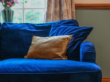 A blue sofa with a brown cushion in a room with a window and floral curtains at Manor Cottage in Northallerton