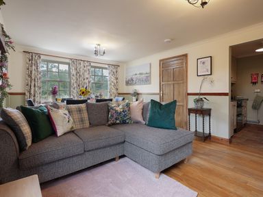 A living room with a gray sectional sofa and patterned cushions near windows with floral curtains at Manor Cottage in Northallerton
