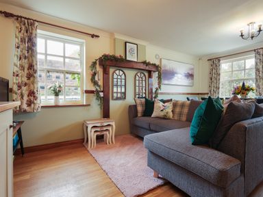 A living room with a gray sectional sofa and floral curtains at Manor Cottage in Northallerton