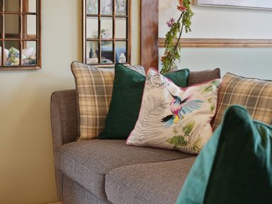 A sofa with green and plaid cushions and a cushion with a bird design at Manor Cottage in Northallerton