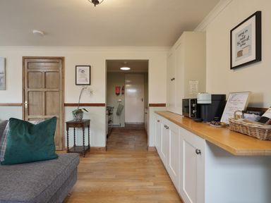 A sitting room with a sofa large green cushion cabinet with coffee machine and basket open doorway leading to kitchen at Manor Cottage in Northallerton