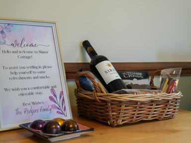 A welcome note beside a basket with wine and snacks on a wooden table at Manor Cottage in Northallerton