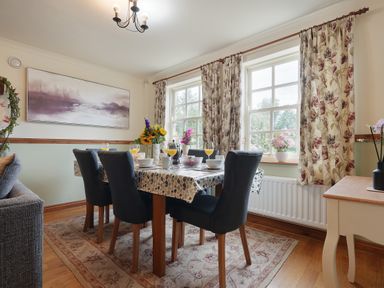 A dining room with a table set for breakfast and floral curtains at Manor Cottage in Northallerton