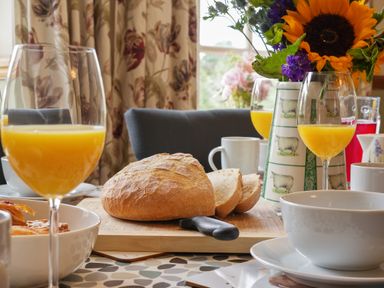 A table set with bread a knife orange juice cups and flowers at Manor Cottage in Northallerton