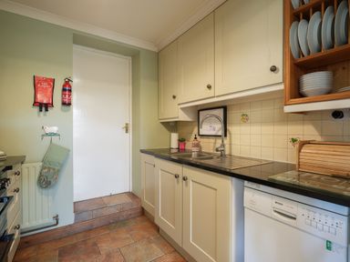 A kitchen with white cabinets a double sink a dishwasher and a white door at Manor Cottage in Northallerton