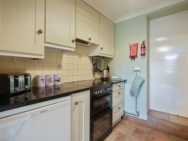A kitchen with cream cabinets black countertop and tiled floor at Manor Cottage in Northallerton