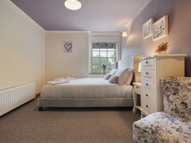 A bedroom with a bed pillows dresser floral chair and a window at Manor Cottage in Northallerton