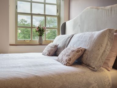 A bedroom with a bed and pillows next to a window with flowers in a vase at Manor Cottage in Northallerton