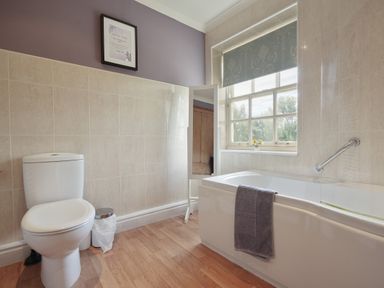 A bathroom with a toilet bathtub with gray towel floor mirror and window at Manor Cottage in Northallerton
