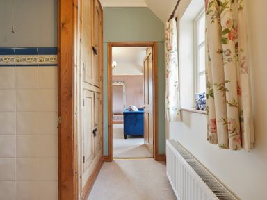 A hallway with wooden cupboards, a window with floral curtains and a radiator looking into a room with a blue sofa at Manor Cottage in Northallerton