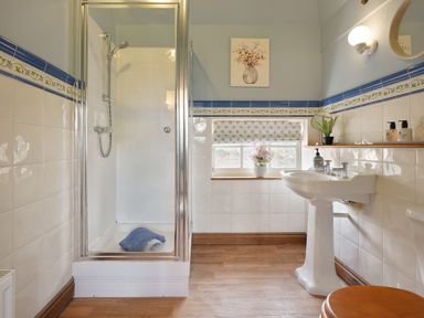 A bathroom with a shower enclosure, pedestal sink, toilet with wooden seat, and small window at Manor Cottage in Northallerton