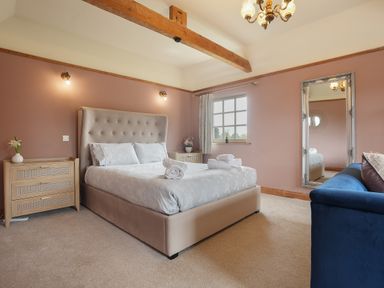 A bedroom with a large bed between two wooden nightstands and a blue sofa next to a full-length mirror at Manor Cottage in Northallerton