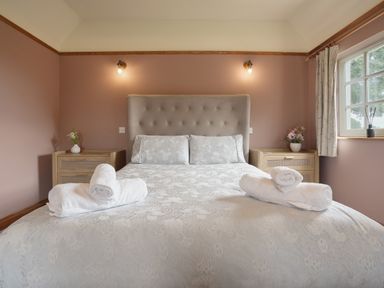 A bedroom with a bed two bedside tables flowers on the tables and a window at Manor Cottage in Northallerton