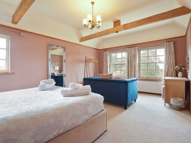 A bedroom with a bed, blue sofa, full-length mirror, wooden hanging rack, wooden dresser, and two windows at Manor Cottage in Northallerton
