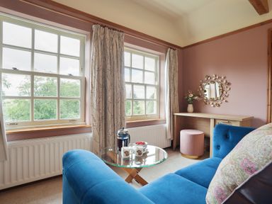 A sitting area with a blue sofa and a glass coffee table near two windows at Manor Cottage in Northallerton