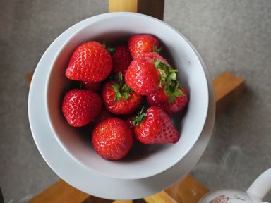 A bowl of strawberries on a white saucer on a wooden surface at Manor Cottage in Northallerton