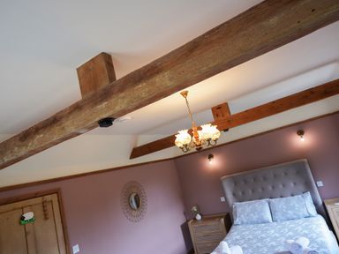 A bedroom with exposed wooden beams a bed with light bedding two bedside tables and a decorative wall mirror at Manor Cottage in Northallerton
