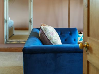 A blue upholstered sofa with patterned cushions in a room with a beige carpet and a large mirror on the wall at Manor Cottage in Northallerton