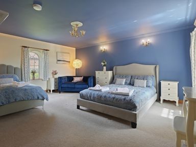 A bedroom with two beds a blue sofa a white dresser and a chair at Manor Cottage in Northallerton