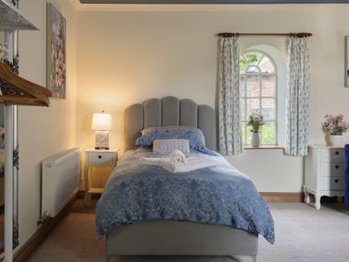 A bedroom with a single bed with blue patterned bedding and a rolled towel on top at Manor Cottage in Northallerton