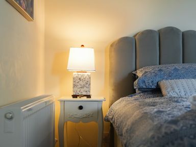 A bedside table with a lamp next to a bed with a padded headboard at Manor Cottage in Northallerton