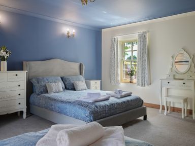A bedroom with a bed and blue bedding beside a white dresser and a vanity at Manor Cottage in Northallerton