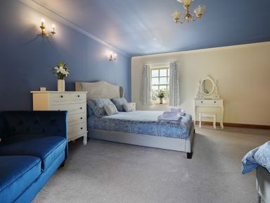 A bedroom with a blue wall bed a blue sofa dresser with flowers and a vanity with a mirror at Manor Cottage in Northallerton