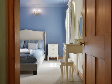 A bedroom with a blue wall a bed with blue bedding a white nightstand and a white dressing table with stool at Manor Cottage in Northallerton