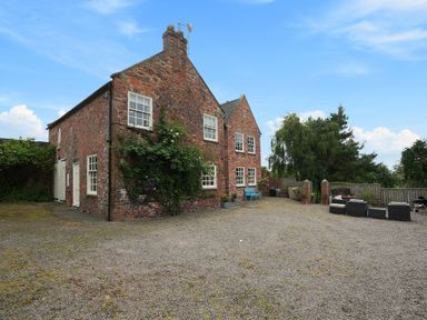 A brick house with white windows and doors surrounded by gravel and outdoor seating at Manor Cottage in Northallerton