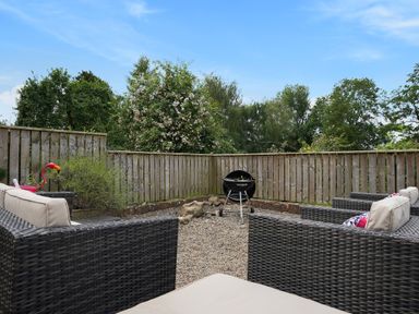 An outdoor seating area with wicker furniture cushions and a charcoal grill in a fenced gravel yard at Manor Cottage in Northallerton