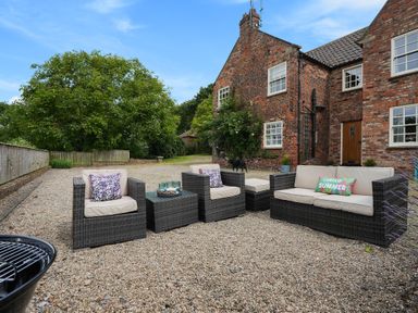An outdoor seating area with wicker chairs and sofa on gravel in front of a brick house at Manor Cottage in Northallerton