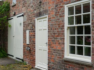 A brick exterior wall with a white door double white garage doors and a window with panes at Manor Cottage in Northallerton